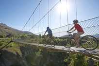 Couple crossing rope bridge on bikes